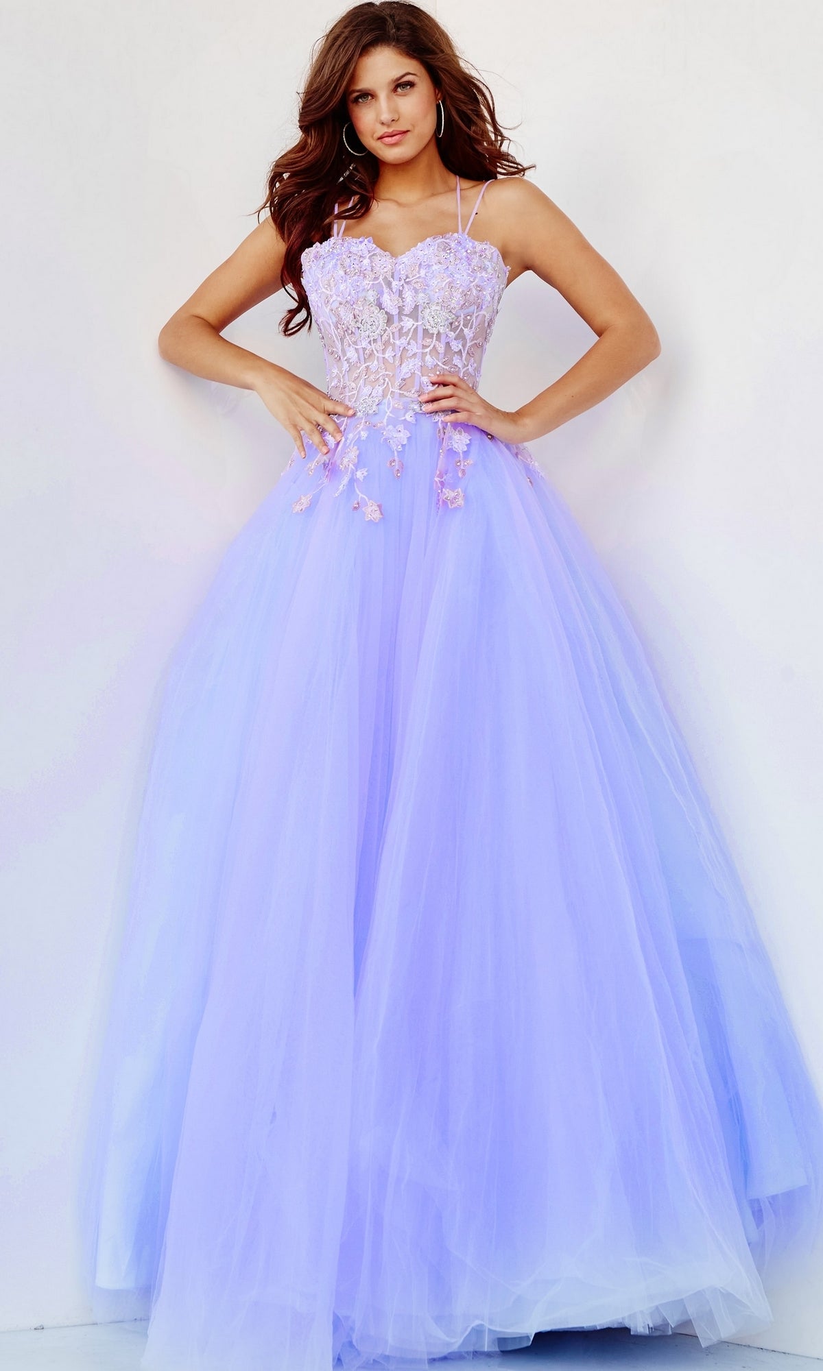 A woman models the Lilac Purple Sheer-Bodice Prom Ball Gown by Jovani, which features a fitted lace bodice and flowing tulle skirt, set against a plain white background.